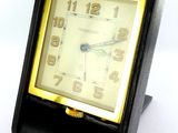 une petite horloge noire avec un cadran jaune sur un fond blanc