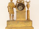 a gold clock with a man standing next to it