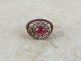 a close up of a ring with a red stone surrounded by diamonds