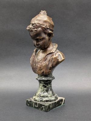 un buste en bronze représentant une femme coiffée d'un chapeau, posé sur un socle