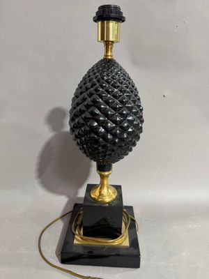 a black and gold table lamp with a pine cone on top