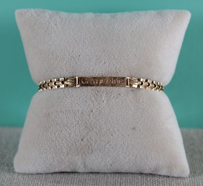 a gold bracelet with a name engraved on it sitting on top of a pillow