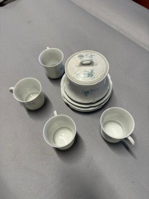 Plusieurs tasses et soucoupes sont posées sur une table, à côté d'une théière.