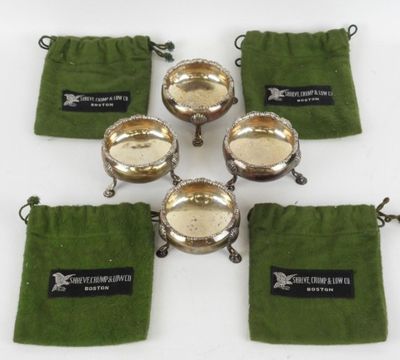 six bols plaqués argent, accompagnés de pochettes en velours vert, posés sur un fond blanc