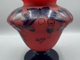 un vase rouge avec un socle noir et orné d'un motif de papillon