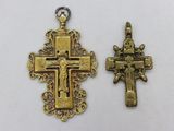 two cross pendants, one gold and one silver, on a white background