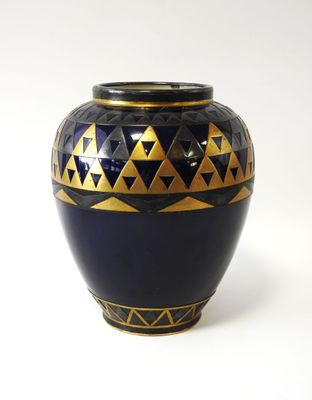 un vase bleu et or posé sur une surface blanche