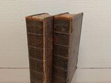 two old books sitting on top of a glass shelf next to a white wall
