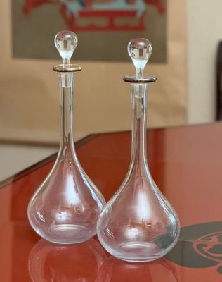 two glass decanters sitting on a table with a picture in the background