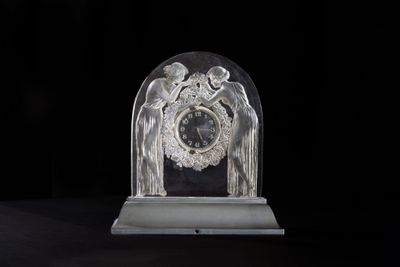 a glass clock with angels on it sitting on a table