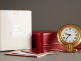 une horloge dorée posée à côté d'une boîte rouge et d'une boîte blanche