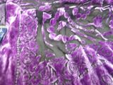 a purple blanket on a bed with a remote in it