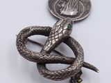 an image of a silver snake broochle with a coin in the background