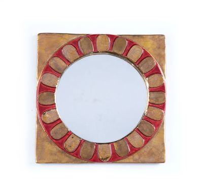 un miroir rouge et doré posé sur une surface blanche