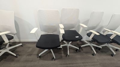 quatre chaises de bureau alignées, avec une assise noire et un dossier blanc