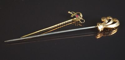 une broche dorée et rouge et une paire de ciseaux posés sur une surface noire