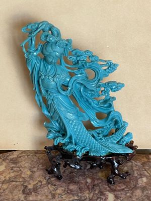 statue d'une femme tenant un poisson, posée sur un socle reposant sur une surface en marbre