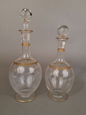 paire de carafes en verre transparent ornées de bordures dorées, posées sur des socles