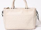 the white handbag has a woven handle and a metal handle