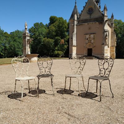 trois chaises et une table devant un bâtiment sur lequel se trouve une horloge