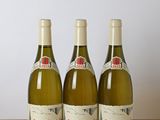 trois bouteilles de vin blanc posées sur une table en bois, à côté d'une bouteille de vin
