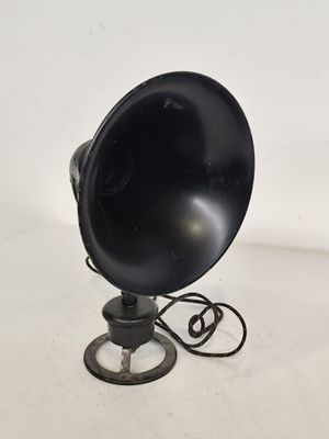 une enceinte noire de style rétro posée sur un pied métallique, elle-même posée sur une surface blanche