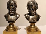 une paire de bustes en bronze représentant deux hommes, posés sur des socles disposés sur une table