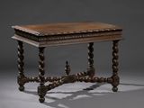 une vieille table en bois dont le plateau est sculpté, sur fond gris