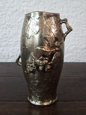 a silver vase on a wooden table with a white wall in the background
