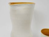 a white vase and a yellow cup sitting next to each other