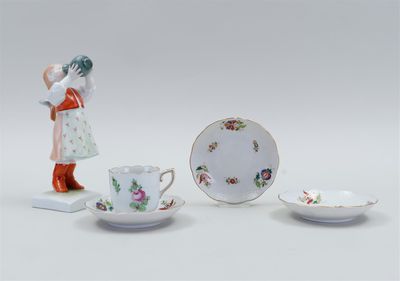 three porcelain figurines of a woman and two cups and saucers