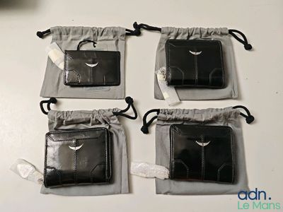 Trois portefeuilles en cuir noir sont posés sur une table blanche