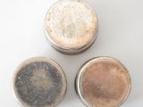 three tins of different colored paint sitting on top of a white surface