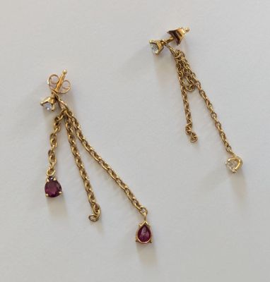 une paire de boucles d'oreilles en or et rubis posées sur un fond blanc