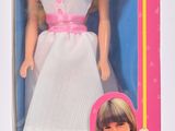 une poupée Barbie dans une boîte rose, vêtue d'une robe blanche et de chaussures roses