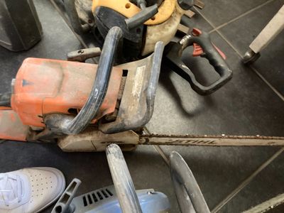 une tronçonneuse posée par terre à côté d'une paire de chaussures