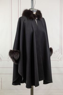 une cape noire à col en fourrure posée sur un présentoir pour mannequin