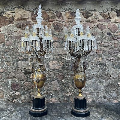 une paire de chandeliers en cristal et en laiton posés sur des socles devant un mur de pierre