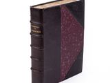 an old book with a purple cover sitting on top of a white surface