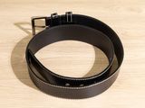 black leather belt with silver buckle on a wooden surface