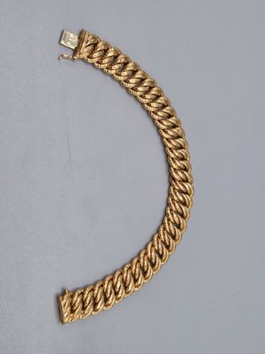 gros plan d'un bracelet en chaîne en or sur une surface grise