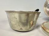 a silver bowl with a spoon in it next to a silver plate