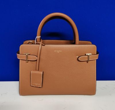 a tan handbag on a table against a blue wall