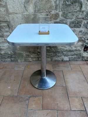 une table blanche avec un plateau en verre, posée sur un sol en briques