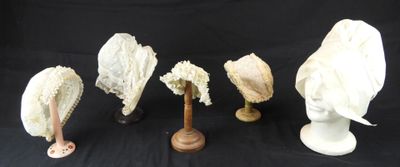 quatre chapeaux blancs sont alignés sur des supports en bois, sur un fond noir