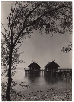 photographie en noir et blanc représentant deux cabanes situées au bord d'un plan d'eau