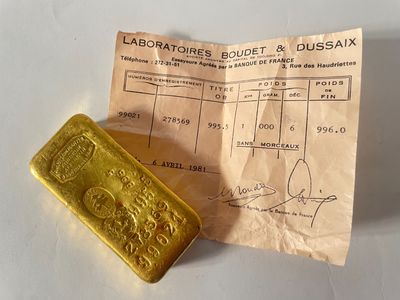 un lingot d'or jaune posé à côté d'un ticket de caisse sur une table blanche