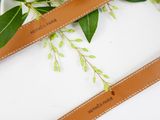 two brown leather belts with green leaves on them on a white surface