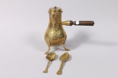 une cafetière dorée avec des cuillères et un repose-cuillères posée sur une surface blanche