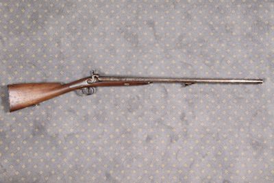 Le fusil est posé par terre, près du mur.